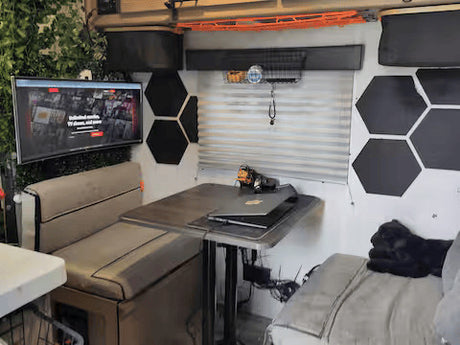 RV rental's modern interior features a dinette, TV, laptop setup, hexagonal decor, and a black dog on a comfy bed.