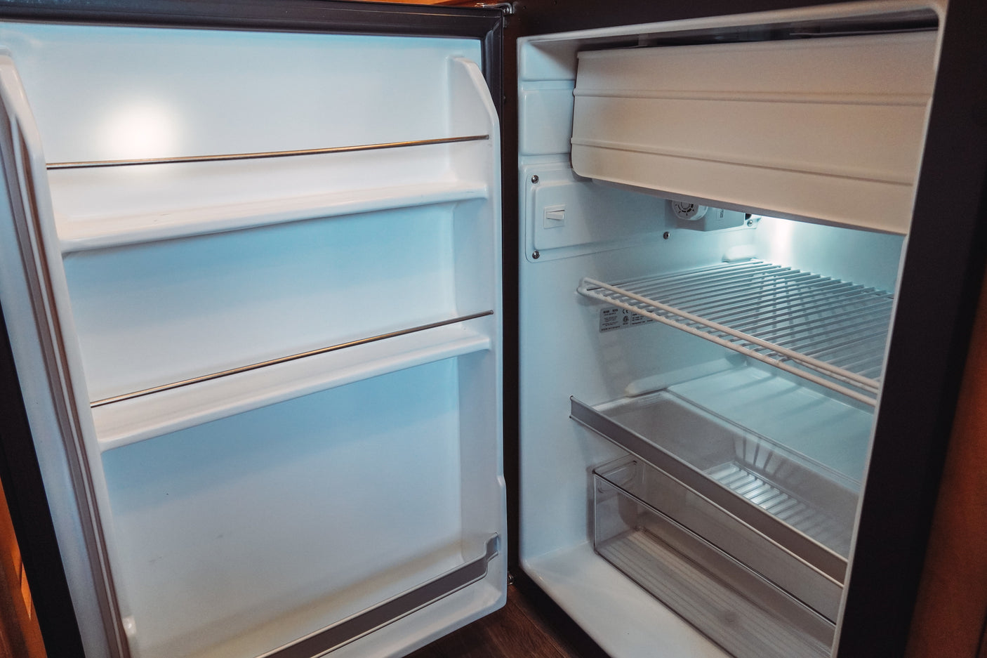 This open, clean, and empty mini-fridge in an RV rental features wire shelves, a freezer, and is ready for your food.