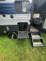 RV rental with door open, revealing a cozy interior, fold-out steps, and an accessible outdoor fridge. Perfect for camping and leisure.