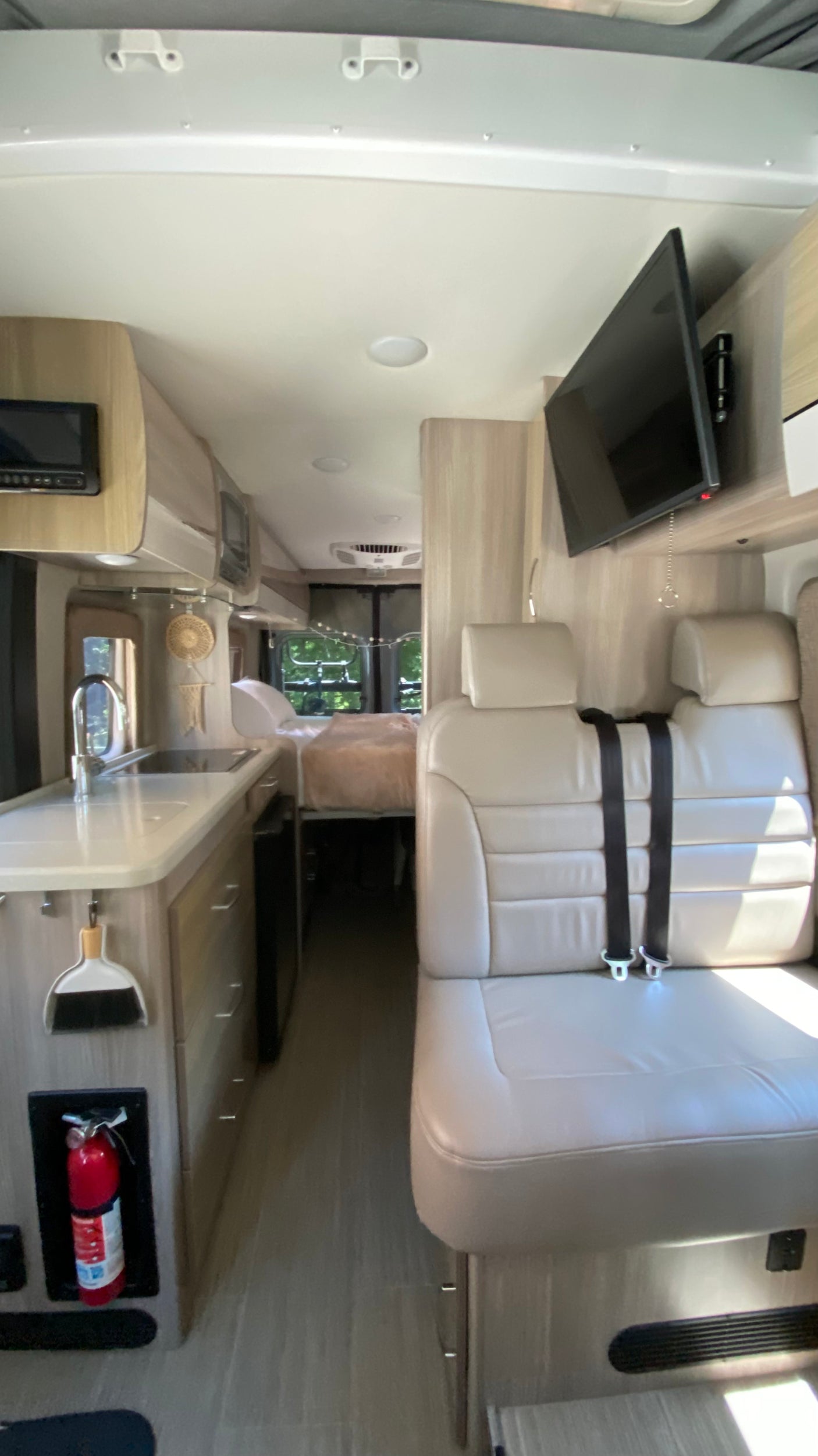 Inside an RV rental: Compact kitchen, comfy seating with seatbelts, TV, and rear bed for your road trip comfort.