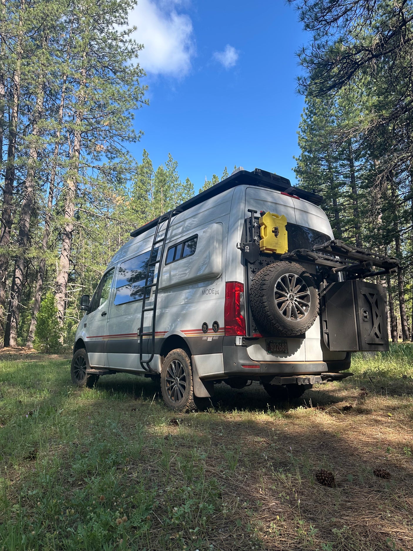 White Sprinter camper van, an ultimate RV rental for forest adventures, parked under blue skies.