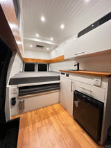 Bright, modern camper van interior for your next RV rental adventure. Features bed, kitchen, fridge, and warm wood accents.