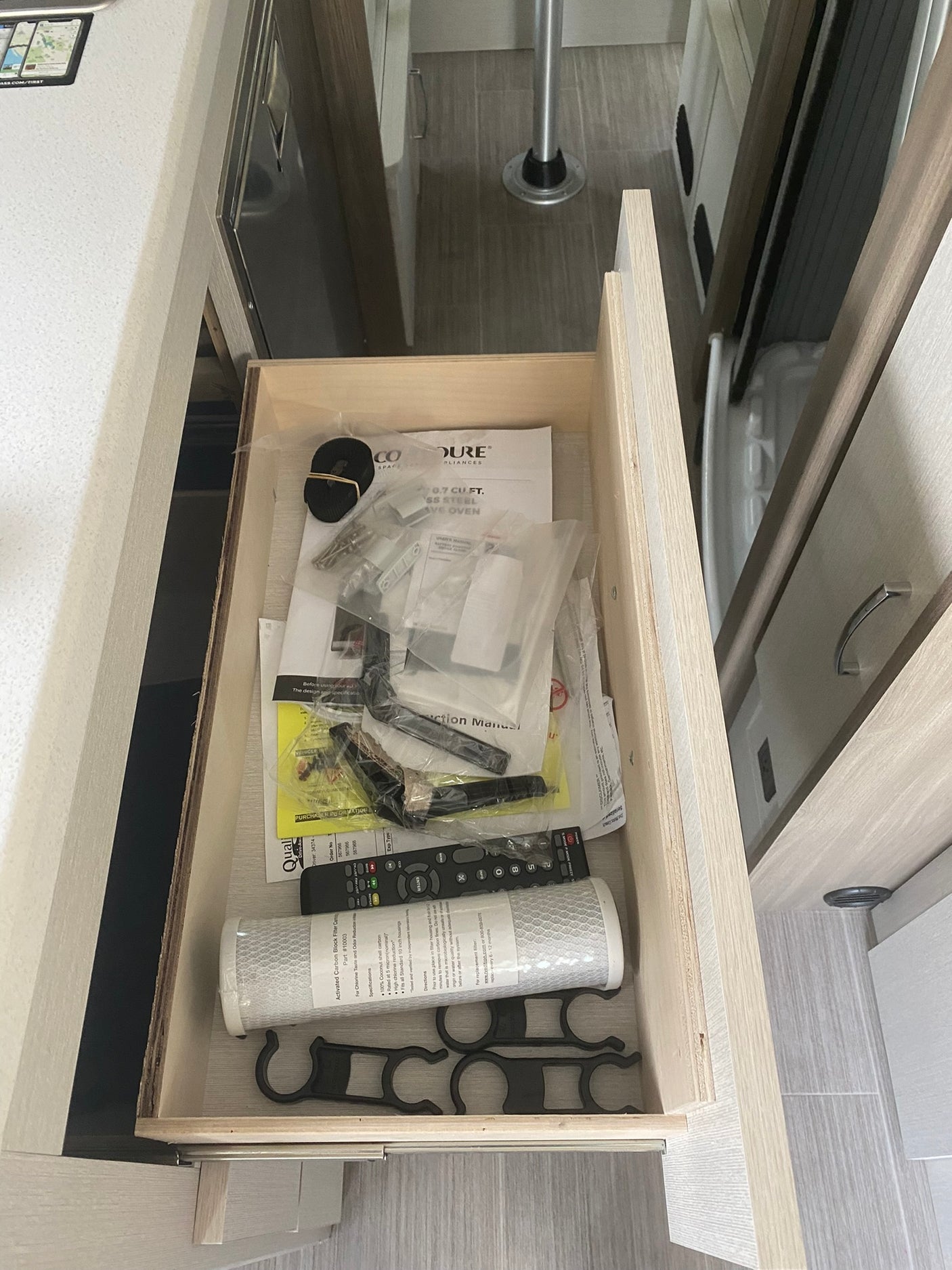 RV rental: Open drawer in modern RV interior with manuals, a water filter, remote control, and new appliance parts.