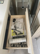RV rental: Open drawer in modern RV interior with manuals, a water filter, remote control, and new appliance parts.