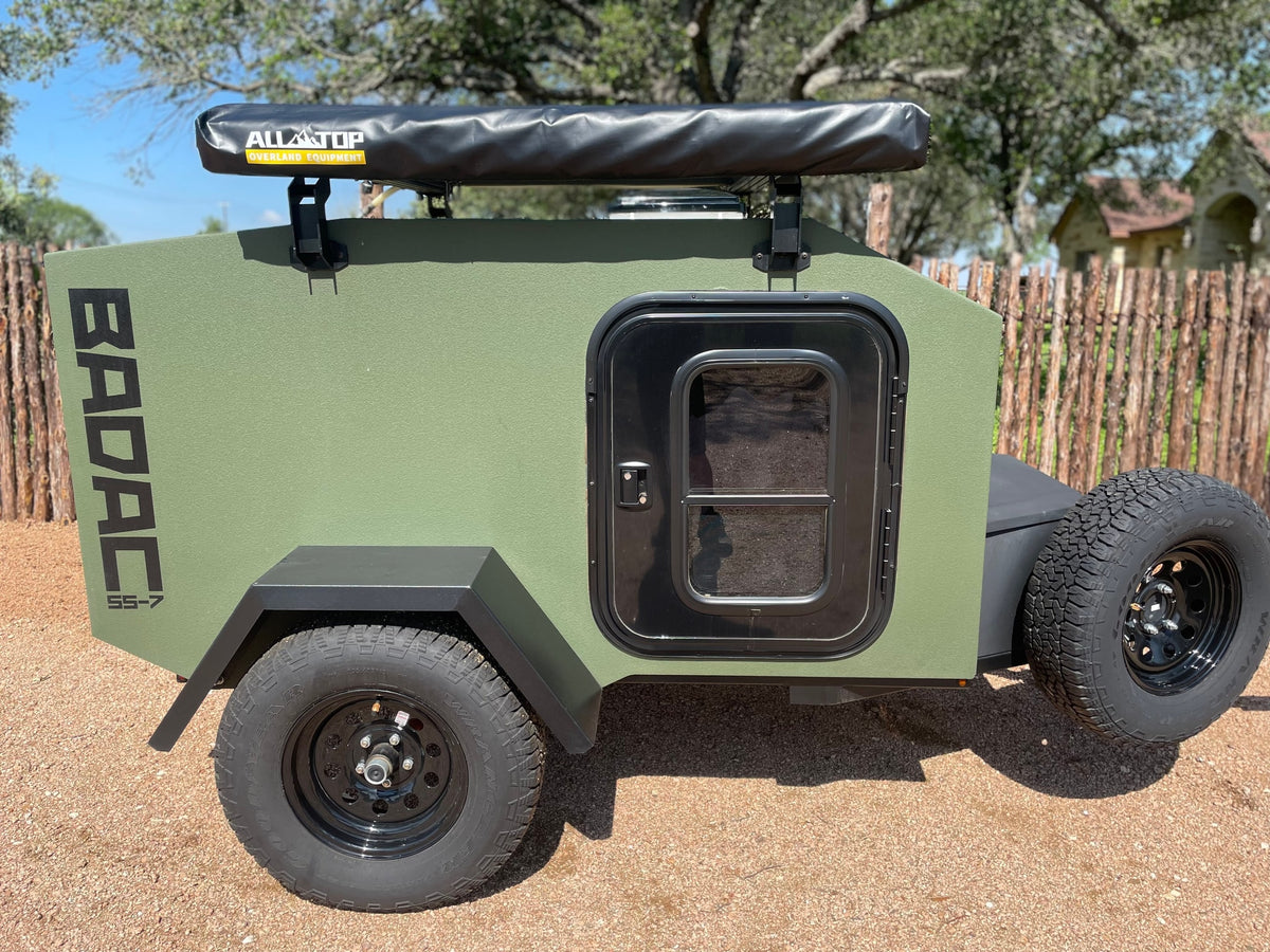 This rugged olive-green BADAC SS-7 off-road RV rental trailer, equipped with an Alltop awning, is ready for your adventure.