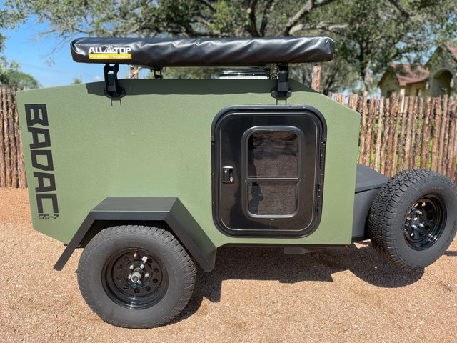This rugged olive-green BADAC SS-7 off-road RV rental trailer, equipped with an Alltop awning, is ready for your adventure.