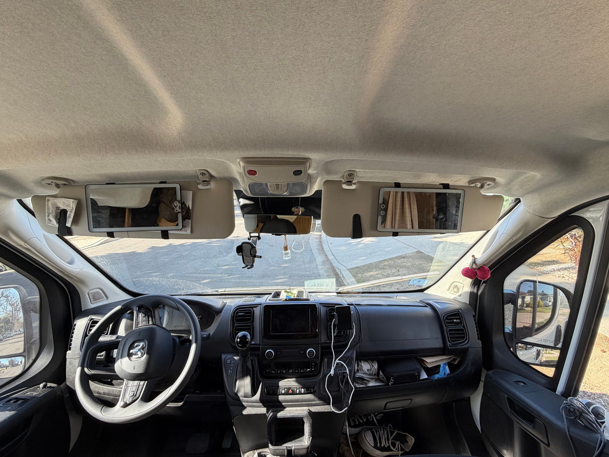 Inside an RV rental: a full view of the front cabin, dashboard, and steering wheel, with sun visors down and personal items visible. — photo 20