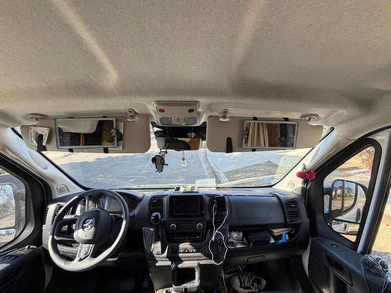 Inside an RV rental: a full view of the front cabin, dashboard, and steering wheel, with sun visors down and personal items visible. — photo 20