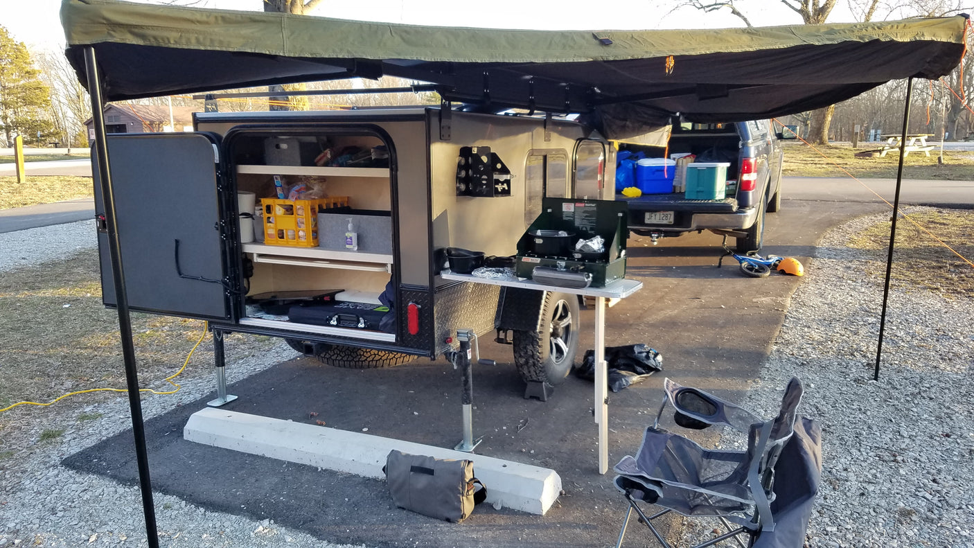 RV rental: Compact camper with outdoor kitchen, awning, and camping gear set up at a scenic campsite. Ready for adventure!