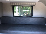 RV rental interior: comfy grey dinette/bed and window reflecting a person, bike, and trees outside.