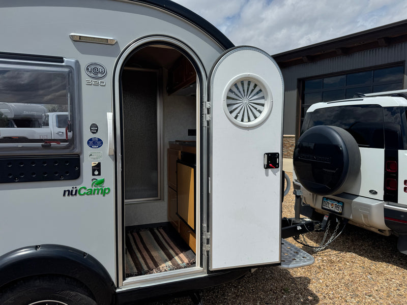 Open door of a nüCamp T@B 320 teardrop camper, revealing its compact interior. It's hitched to a Land Rover Defender, perfect for an rv rental. — photo 9