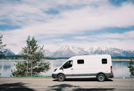 White rv rental campervan parked by a beautiful lake, with majestic snowy mountains in the background. Perfect for outdoor adventures.