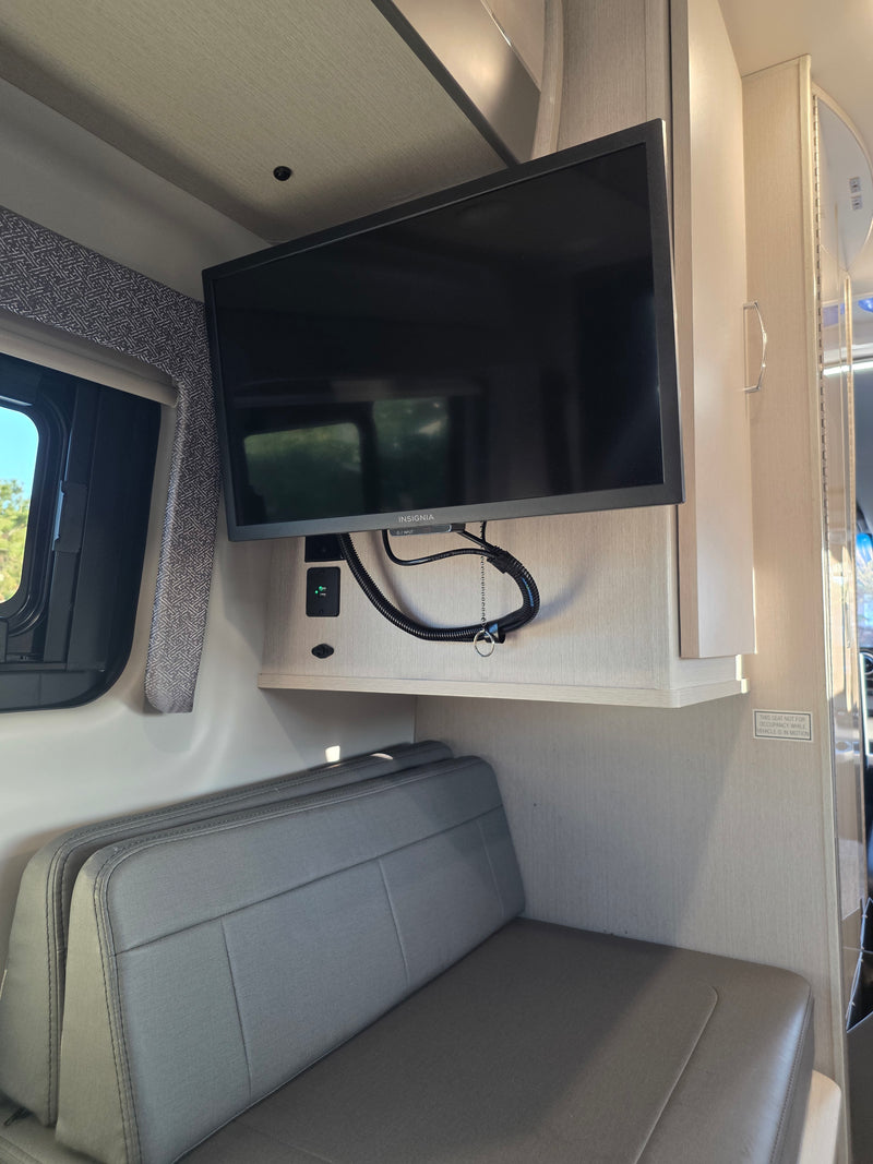 Inside an rv rental: a wall-mounted Insignia TV, USB charging ports, and a grey upholstered bench seat, with a "not for occupancy while in motion" warning visible. — photo 7