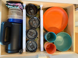 Organized kitchen drawer in an RV rental with an electric kettle, travel mugs, plates, and cups, showing efficient space use for travel.