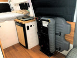 Compact RV rental interior featuring a bed, kitchen with fridge/cooktop, and a foldable seat for versatile living space.