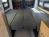 RV rental: Camper van interior with a grey modular bed, rear windows offering natural light, and organized storage on back doors.