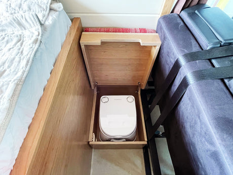 RV rental with a cleverly hidden Dometic portable toilet inside a wooden cabinet, located between a bed and a couch.