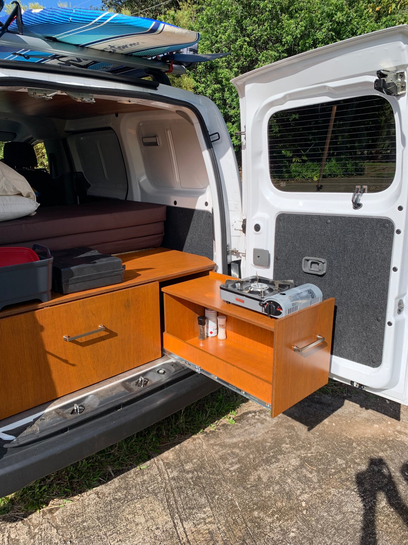 This RV rental shows a camper van's pull-out kitchen with a stove, spices, and a cozy bed inside for camping.