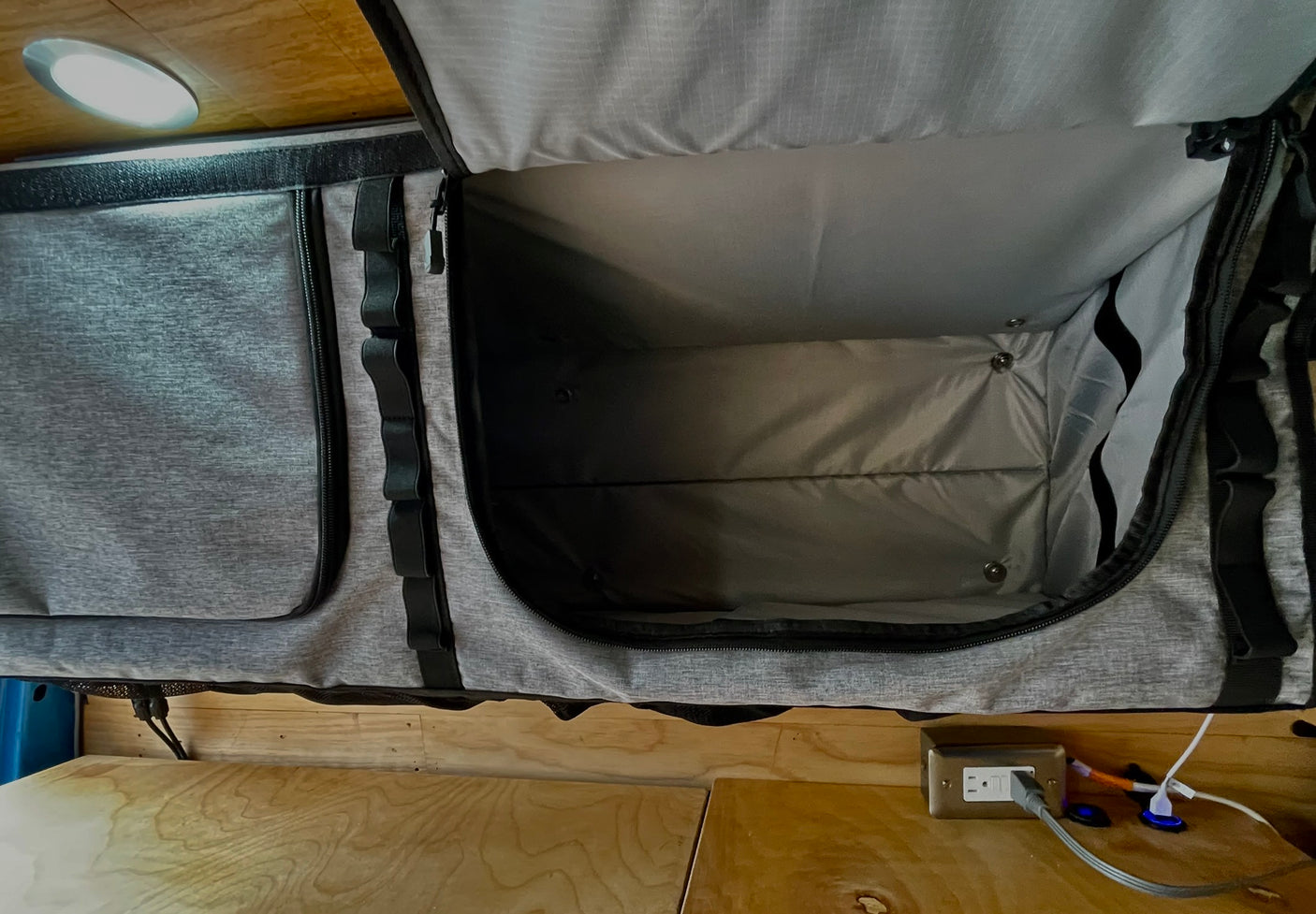 **RV rental** overhead fabric storage bin, open to show its interior. A light is above, and a charging outlet is below on wood.