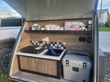 Teardrop RV rental kitchen setup with portable stove, sink, and cooler, perfect for camping and outdoor cooking.