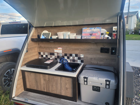Teardrop RV rental kitchen setup with portable stove, sink, and cooler, perfect for camping and outdoor cooking.