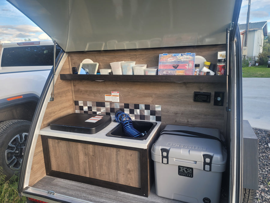Teardrop RV rental kitchen setup with portable stove, sink, and cooler, perfect for camping and outdoor cooking.