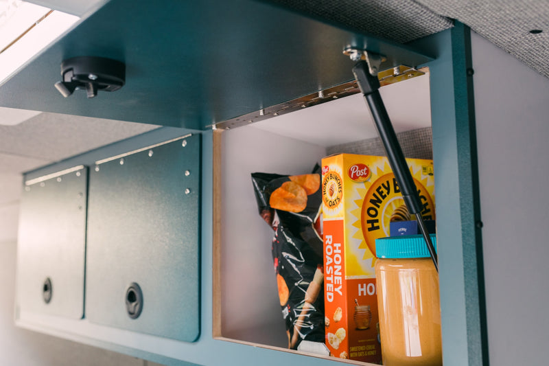 Open overhead cabinet in an RV rental, stocked with Honey Bunches of Oats cereal, chips, and peanut butter for road trip snacks. — photo 8