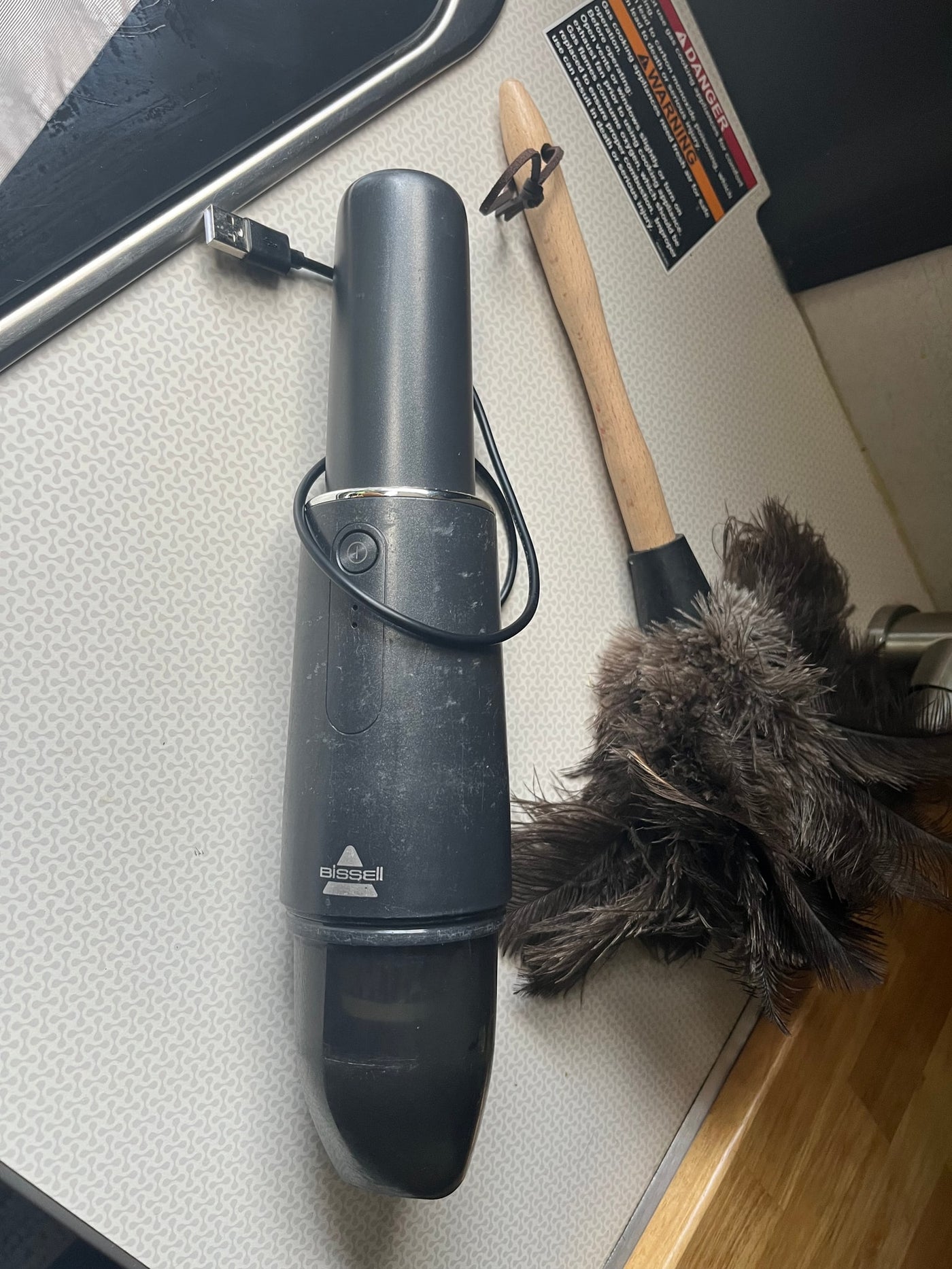 Compact Bissell vacuum & feather duster, essential cleaning tools in an RV rental. Gas appliance warning visible. — photo 18