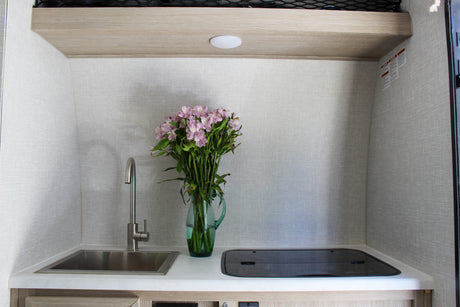 Inside an RV rental: a compact kitchen with a sink, covered cooktop, and a vase of pink flowers.
