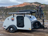 An RV rental teardrop camper with bikes and a roof cargo box sits ready for adventure amidst Utah's red rock mountains.