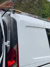 An RV rental van shows a portable roof shower system spraying water across its top, ideal for outdoor cleaning & adventures.