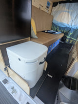 RV rental's clever interior: a slide-out portable toilet, bed with crate storage, and scenic wall decor.