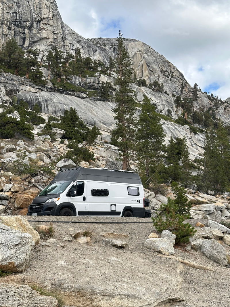A white Noovo RV rental camper van on a mountain road, surrounded by majestic granite cliffs & evergreen trees under a cloudy sky. — photo 3