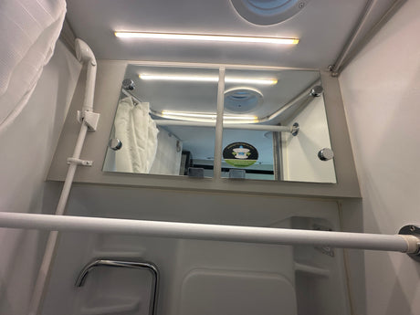 RV rental interior: compact shower/bathroom space with a mirror, shower head, and bright ceiling light.