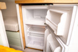 RV rental: Open, empty mini-fridge with freezer, shelves, and ice cube tray in a camper's kitchen.