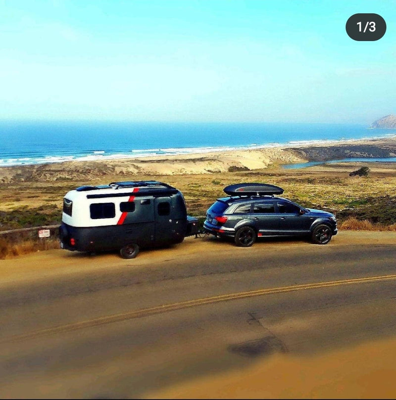 Coastal rv rental adventure: Dark SUV towing a sleek camper on a scenic road overlooking the ocean and beach. — photo 3