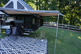 Kick back with this RV rental setup! A modern camper, awning, outdoor kitchen, chairs, and mat on grass for camping.