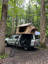 Silver truck with a rooftop tent at a forest campsite. Ideal for outdoor adventures, offering an RV rental alternative.