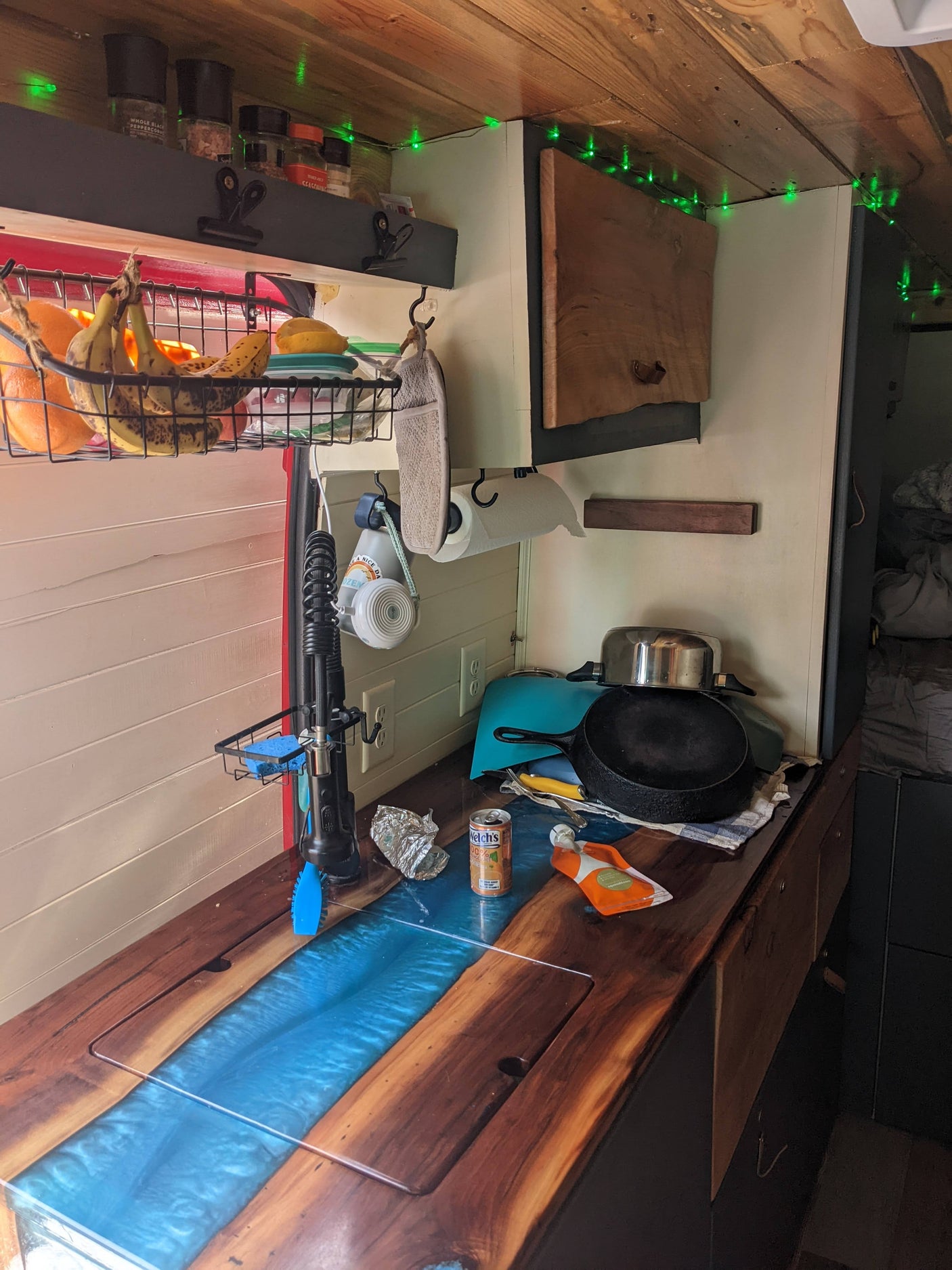 RV rental's cozy mobile kitchen: wood & resin countertop, fresh fruit, spices, cookware, and green lights.