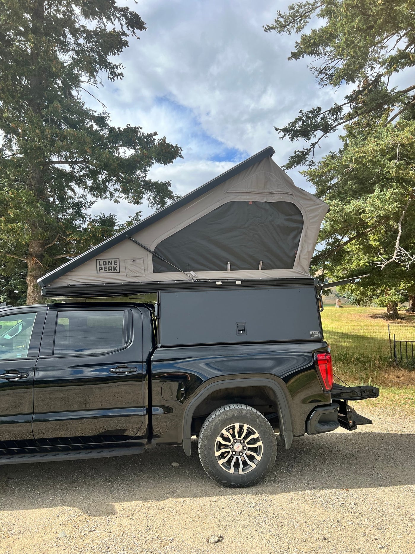 A black pickup truck with a deployed Lone Peak pop-top truck camper, ideal for an outdoor rv rental adventure. — photo 13