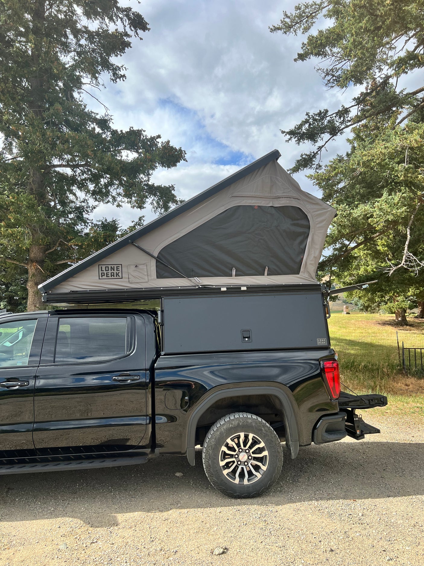 A black pickup truck with a deployed Lone Peak pop-top truck camper, ideal for an outdoor rv rental adventure.