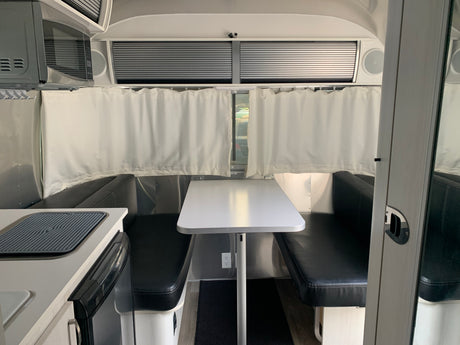 Modern RV rental interior, showing a dining area with black benches, white table, microwave, and kitchen.