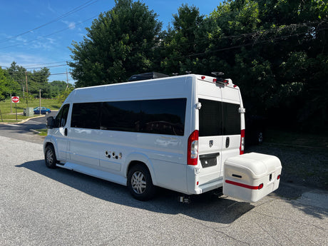 White camper van RV rental, equipped with utility hookups & a rear storage box, parked on asphalt.