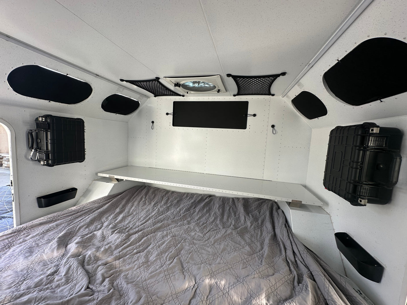 Bright rv rental interior featuring a quilted bed, overhead shelf, wall storage cases, and ceiling fan for comfortable travel.