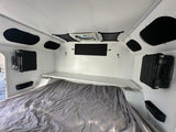 Bright rv rental interior featuring a quilted bed, overhead shelf, wall storage cases, and ceiling fan for comfortable travel.