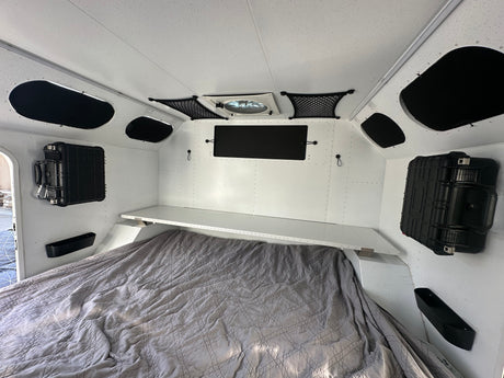 Bright rv rental interior featuring a quilted bed, overhead shelf, wall storage cases, and ceiling fan for comfortable travel.