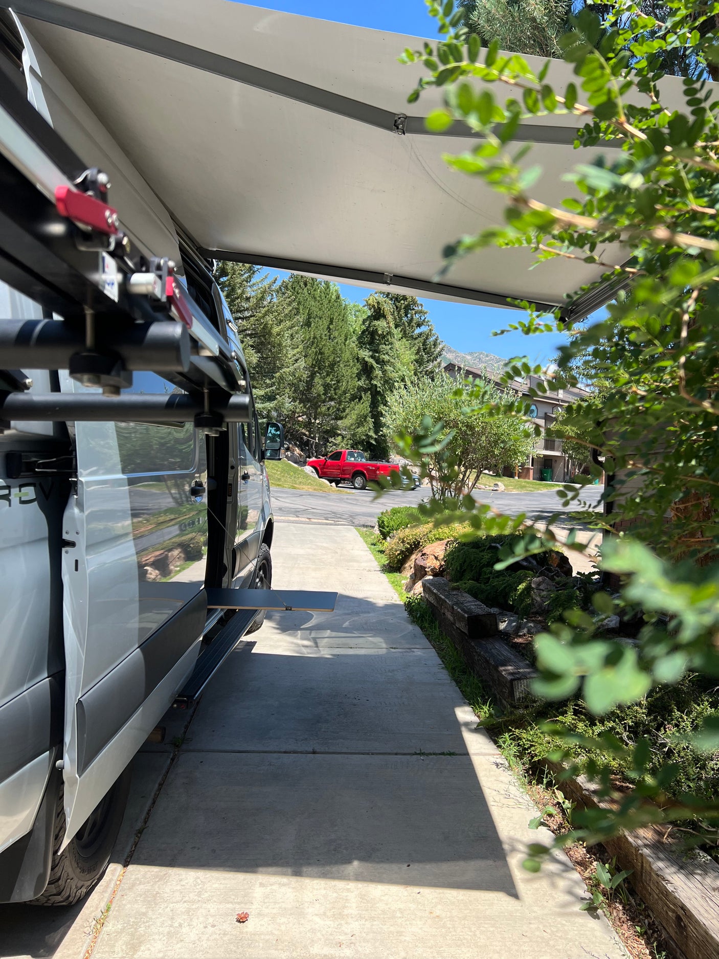 Relaxing outside a modern RV rental with an extended awning and side table, enjoying the mountain view on a sunny day.
