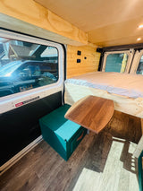 Experience an RV rental! This camper van interior features a bed, wood paneling, movable table, and green storage.