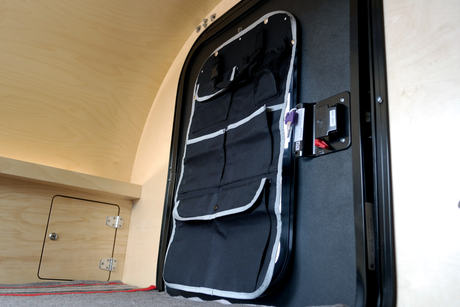 Inside an RV rental: A door-mounted organizer adds storage to the black door, with light wooden walls and a storage hatch.