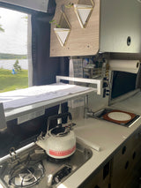 Compact RV rental kitchen with stove, sink, and lake view, perfect for camper adventures.